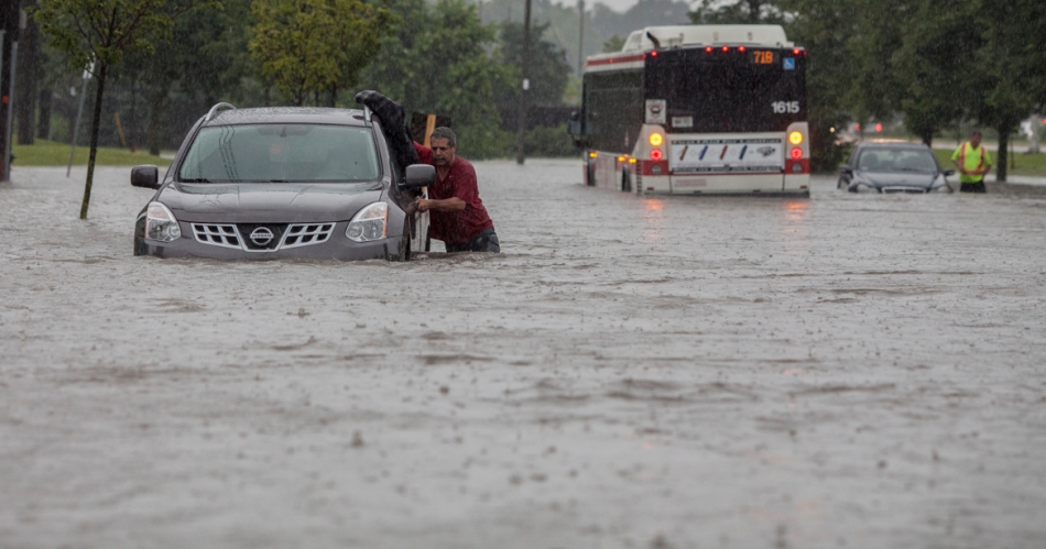 A driver attempts to push his car through a flooded Todd Baylis Blvd near Black Creek Drive and Eglinton Ave West on Monday.  Behind him is a stranded TTC bus and another car.  Shortly before 5pm a sudden and severe thunderstorm swept the Toronto area causing occasional flooding. (July 8, 2013)