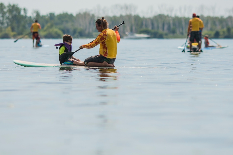 A surfer helps a camper with on a stand-up paddle board during the second day of Aloha Toronto at Cherry Beach on Sunday.  The event, hosted by Surfers Healing Camp is a free camp which pairs up children with autism and professional surfers who teach them how to surf or stand-up paddle. (August 25, 2013)