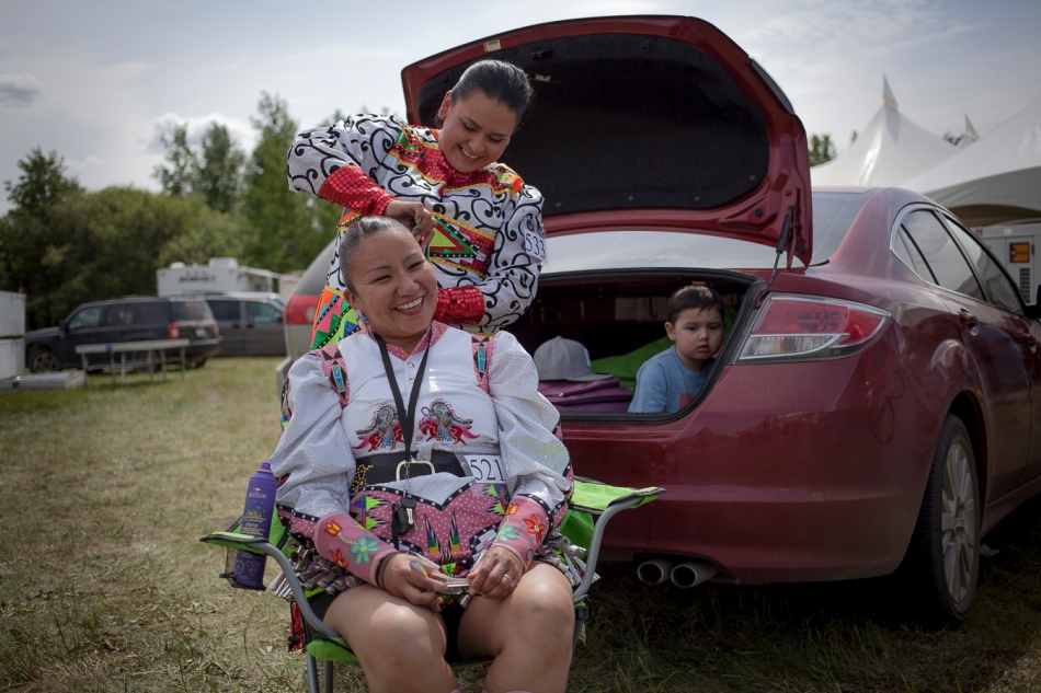 Braider Cyrina Bull, a Cree dancer from Red Pheasant, Sask. braids the hair of Ojibway dancer Rolanda Wilson from Fox Lake, Alta. while Cyrina's son, Bradson Crain watches from the trunk of the car, on the second day of a Pow Wow hosted at the fairgrounds in Peace River Alta. on Sunday, June 15, 2014.  Adam Dietrich | Record-Gazette/QMI Agency